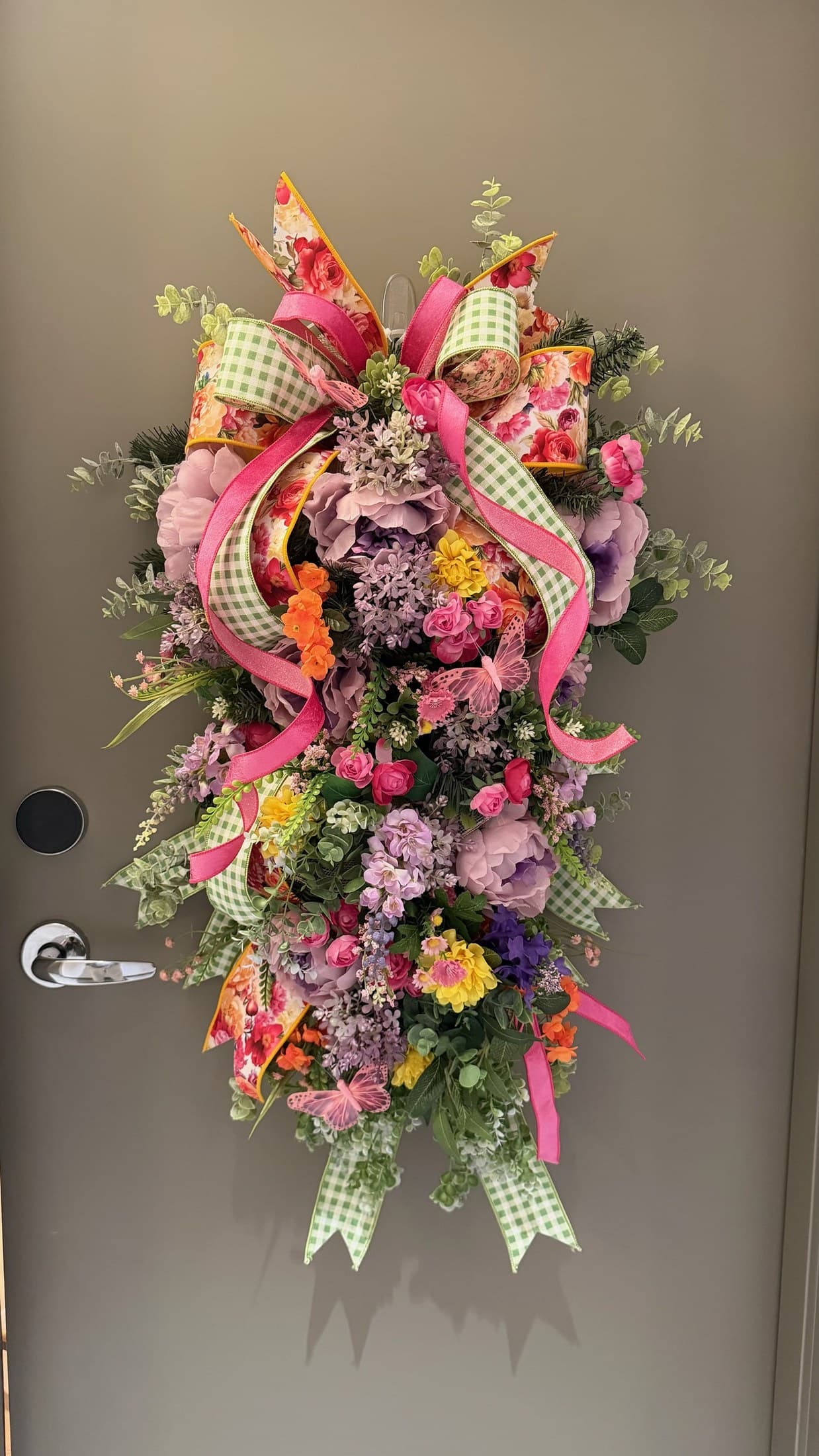 Bright spring floral door swag with pink ribbon, greenery, and colorful blossoms.