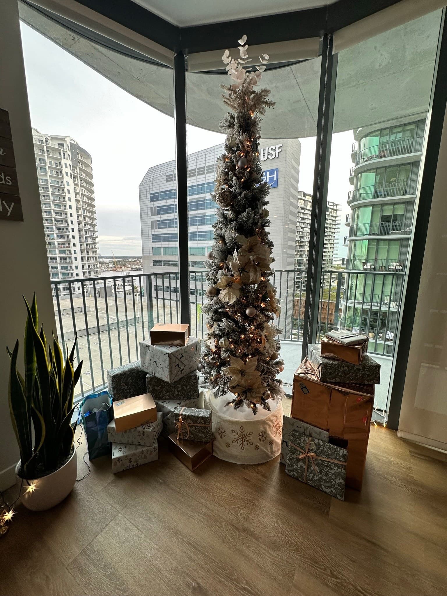 Champagne pencil Christmas tree styled beside city windows with gold ribbon and ornaments.