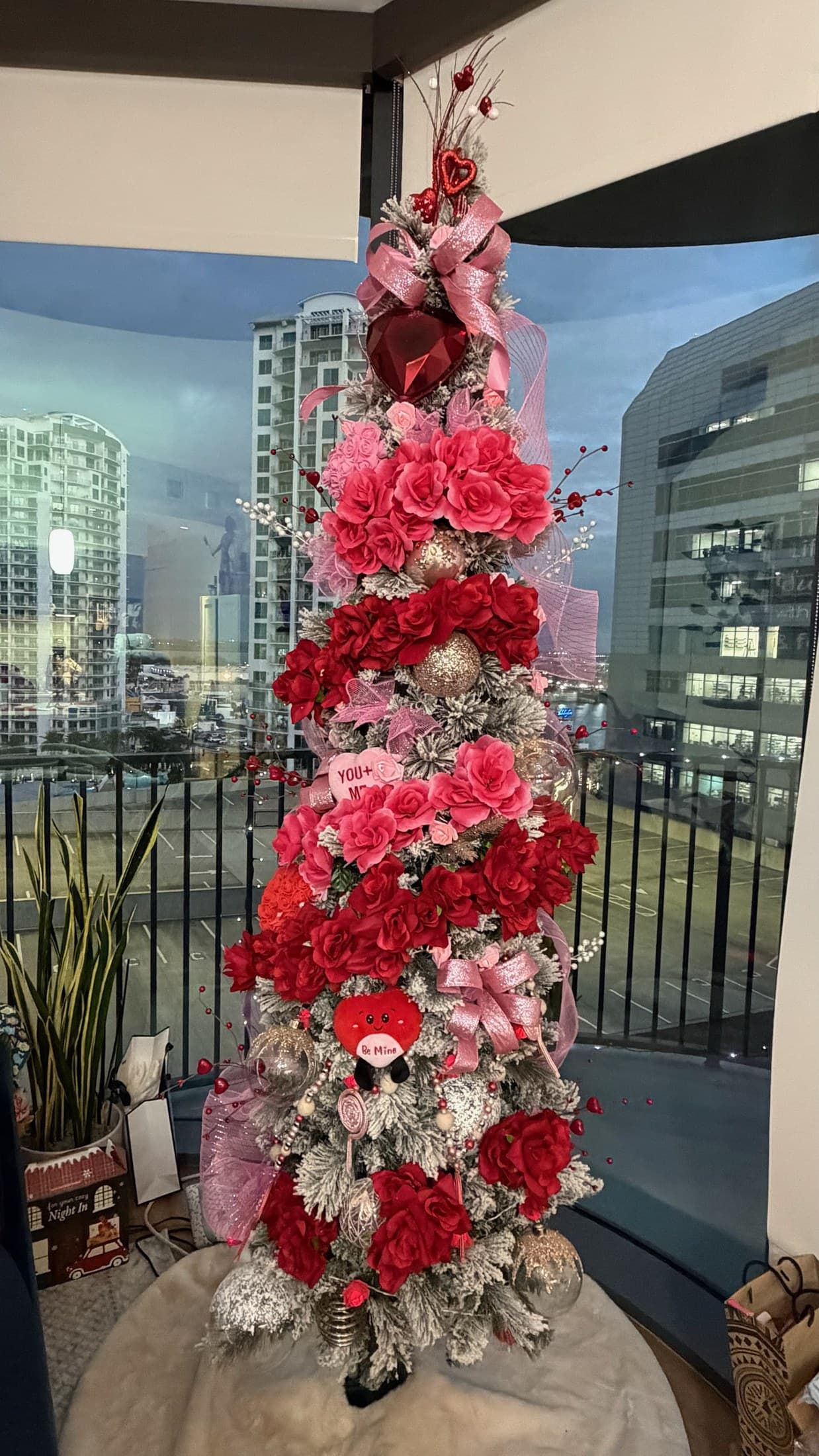 Pink floral Christmas tree with ribbon and ornaments styled in front of a city view.