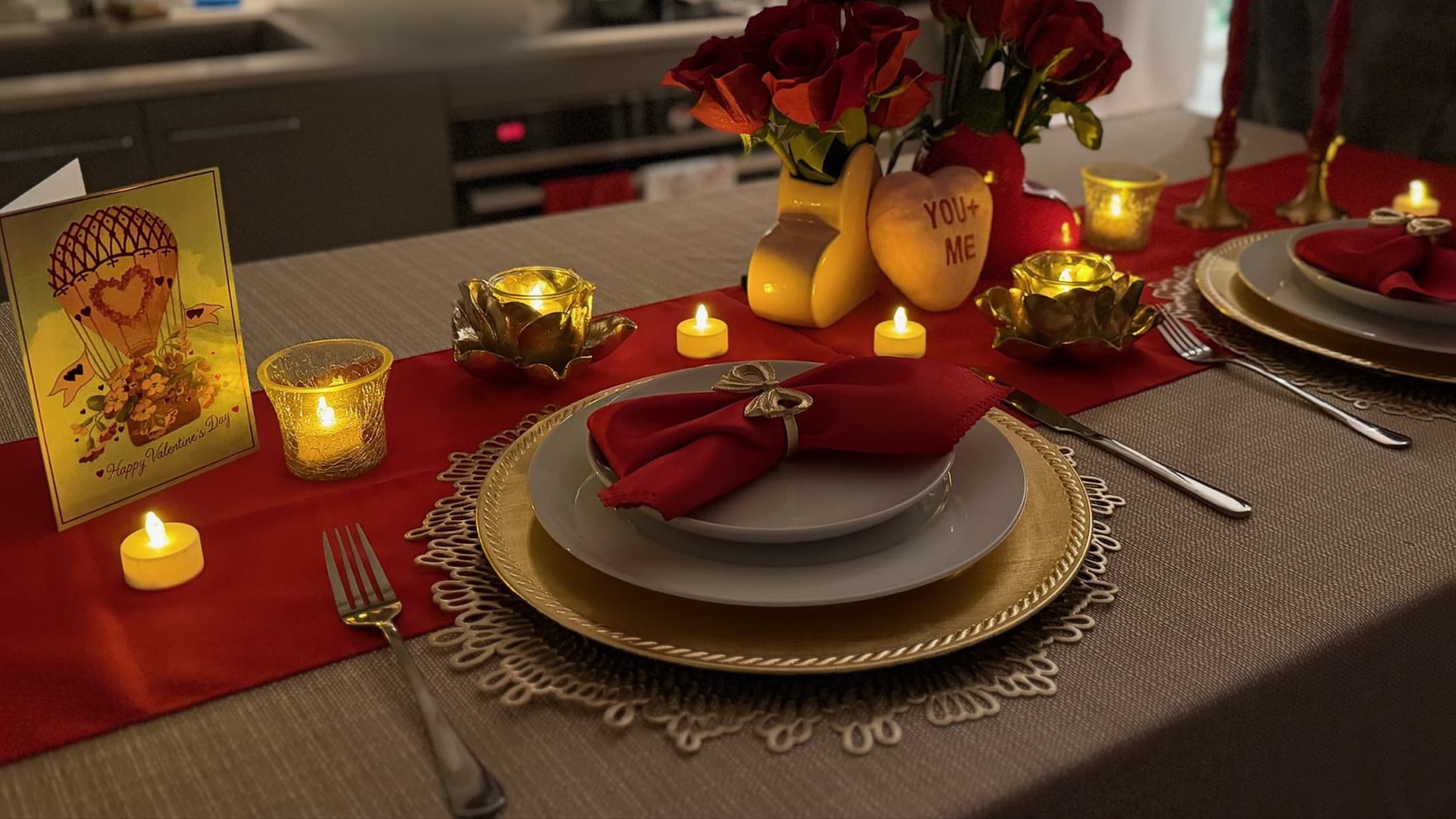 Red and gold holiday tablescape with candles, roses, chargers, and place settings.