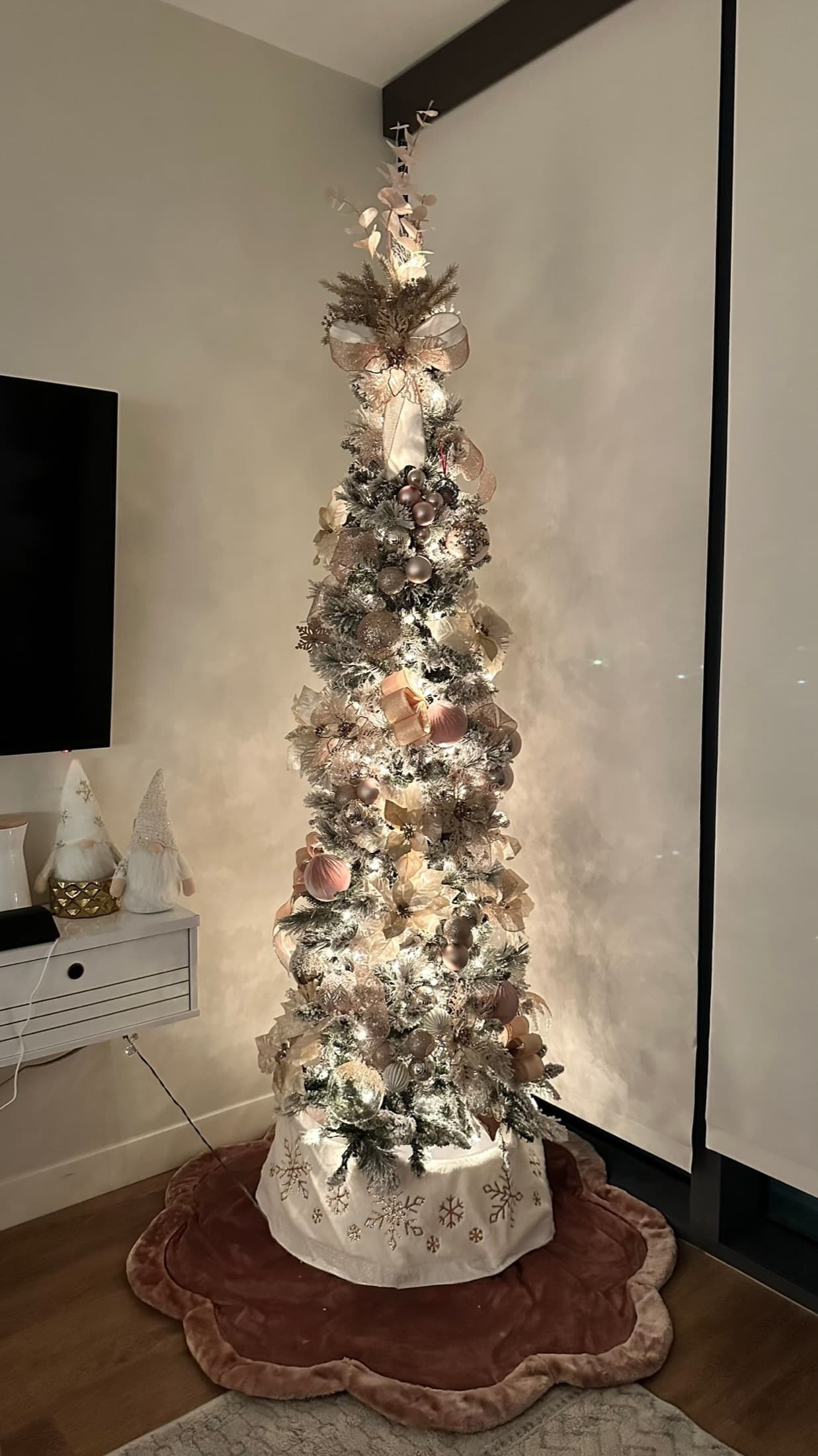 Warm slim Christmas tree styled in a small living room corner with soft lights.